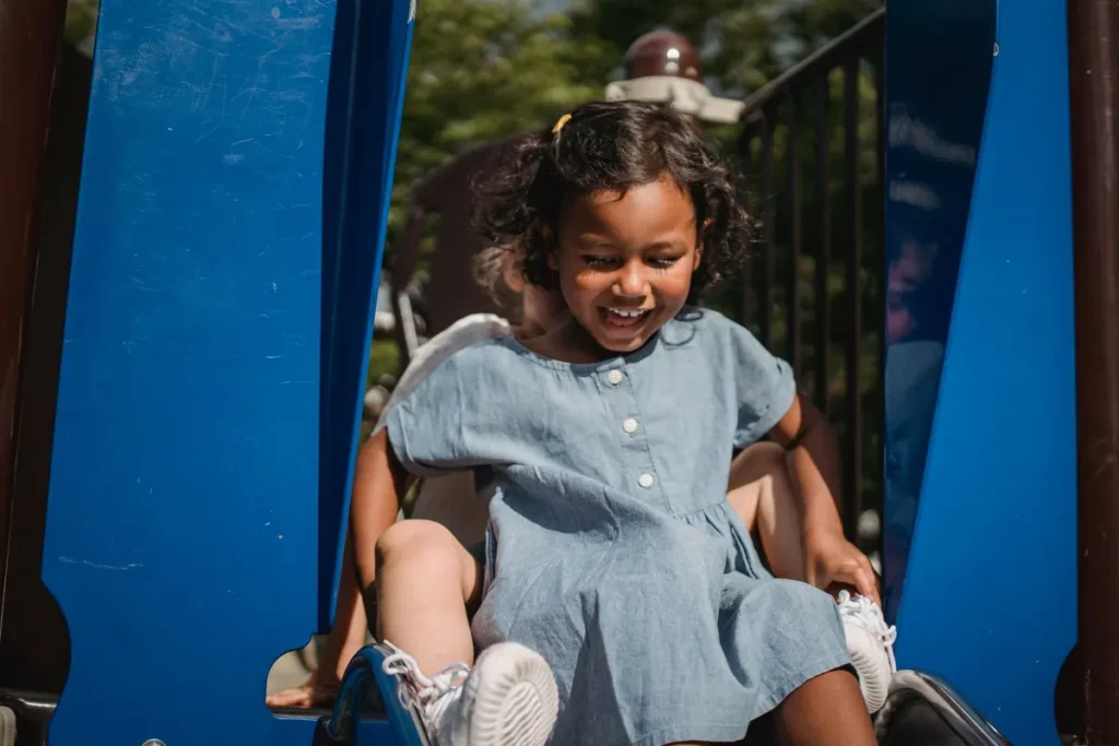Peuter glijdt lachend van een kleine glijbaan in een speeltuin